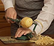 A potato being peeled with a "slinky" apple peeler.