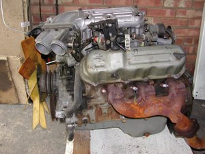 Left side of a Ford Cologne V6 engine, clearly showing a (rusty) cast iron exhaust manifold - three exhaust ports into one pipe.